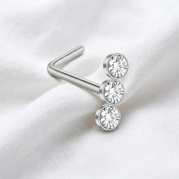 Clou en L argente 3 zircons bezel — pose sur tissu blanc