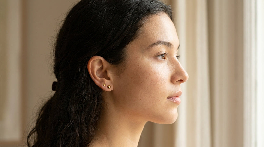 Femme de profil portant deux piercings dorés au lobe de l'oreille
