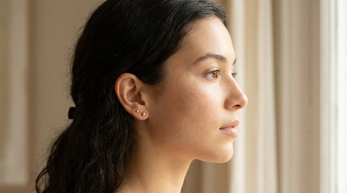Femme de profil portant deux piercings dorés au lobe de l'oreille