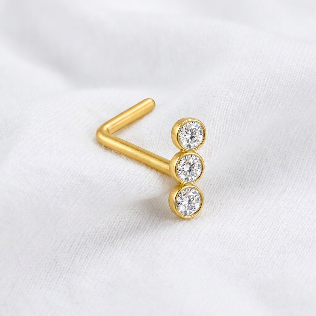 Clou en L dore 3 zircons bezel — pose sur tissu blanc