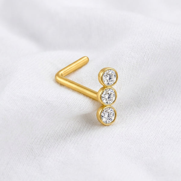 Clou en L dore 3 zircons bezel — pose sur tissu blanc