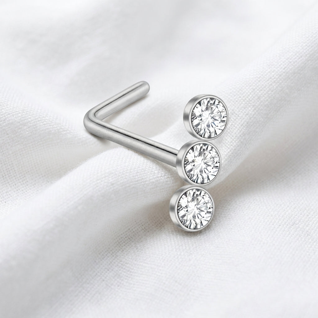 Clou en L argente 3 zircons bezel — pose sur tissu blanc