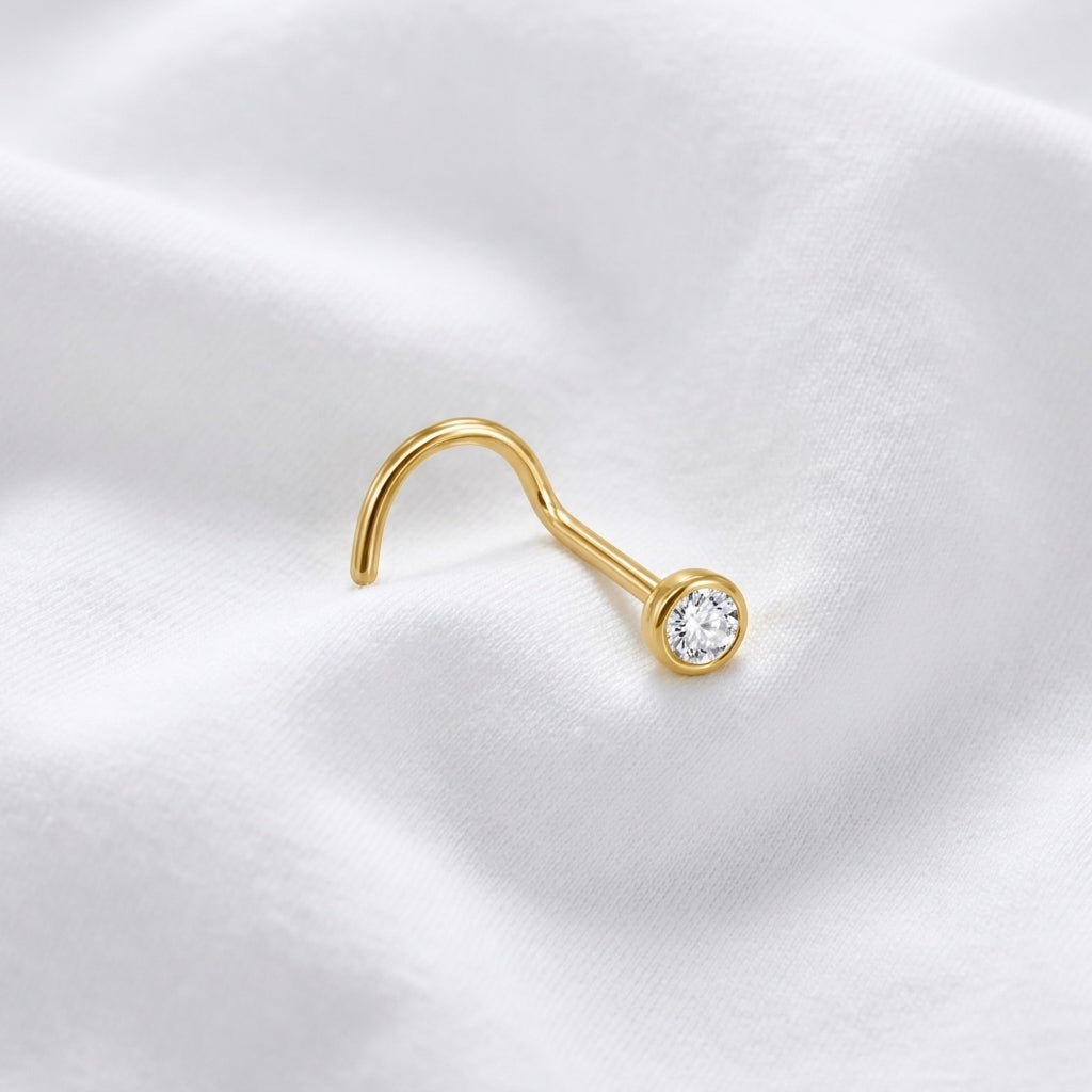 Vis nez doree zircon rond sertissage bezel — macro pose tissu blanc inclinee